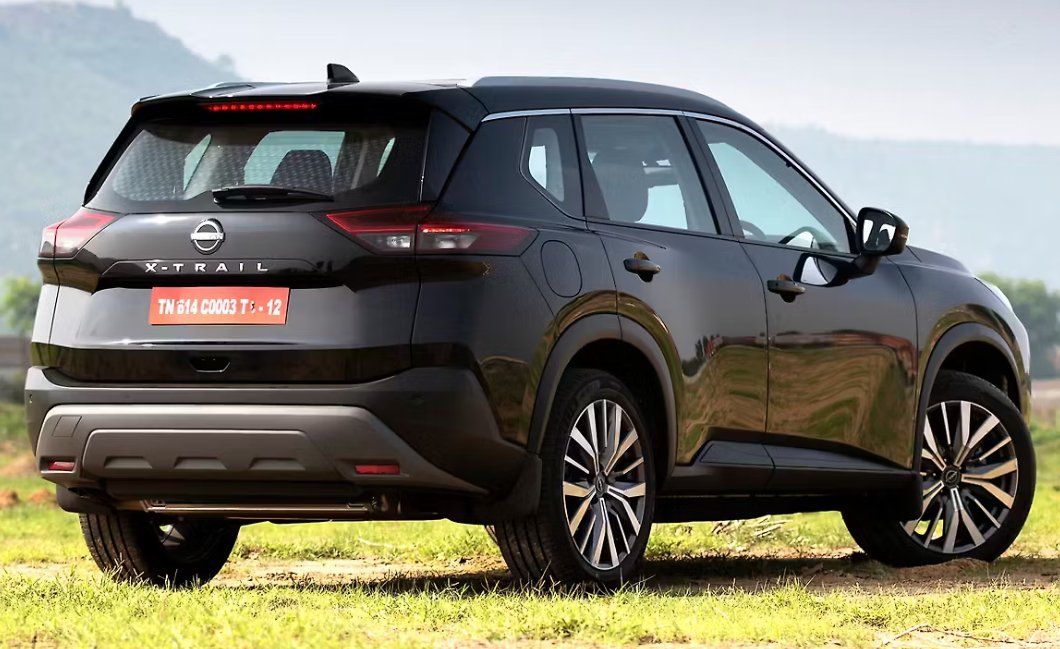 Black Nissan X-Trail SUV parked on grass with mountains in background.