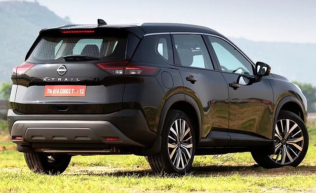 Black Nissan X-Trail SUV parked on grass with mountains in background.