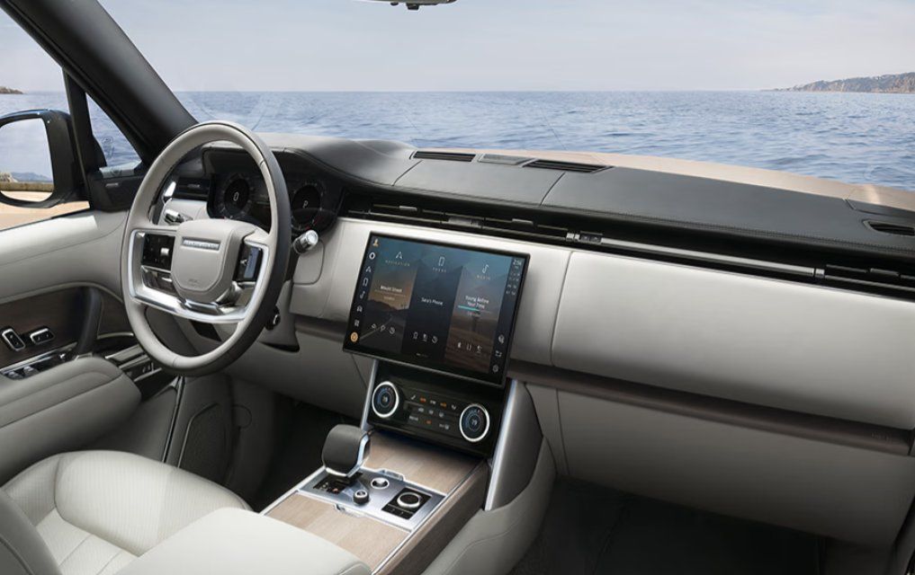 Modern vehicle interior with touchscreen display, steering wheel, and ocean view through windshield.