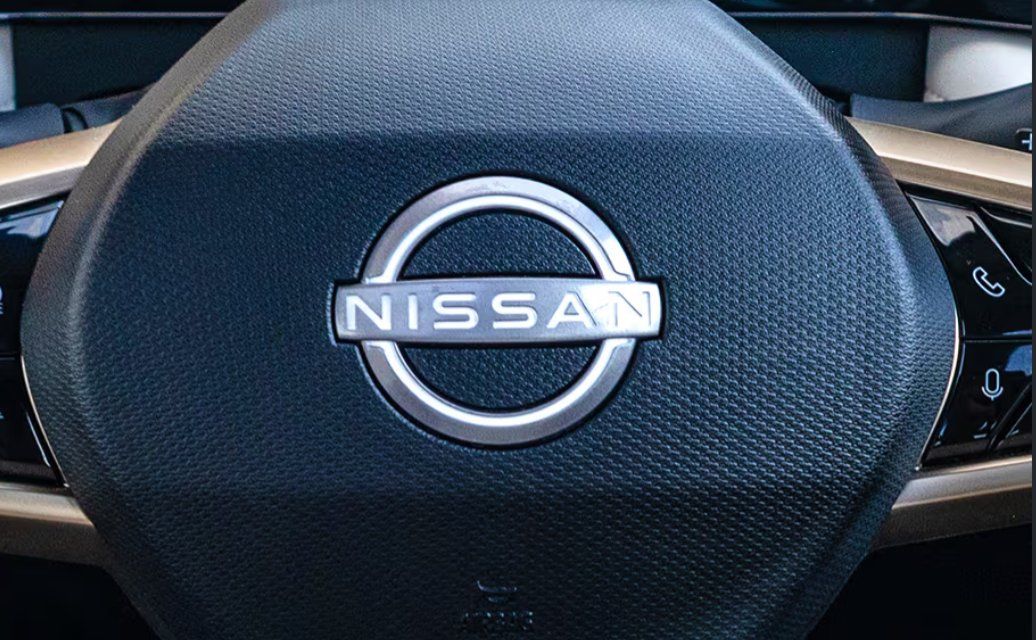 Nissan steering wheel airbag cover with chrome badge and textured dark fabric.