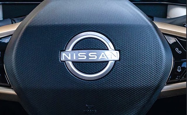 Nissan steering wheel airbag cover with chrome badge and textured dark fabric.