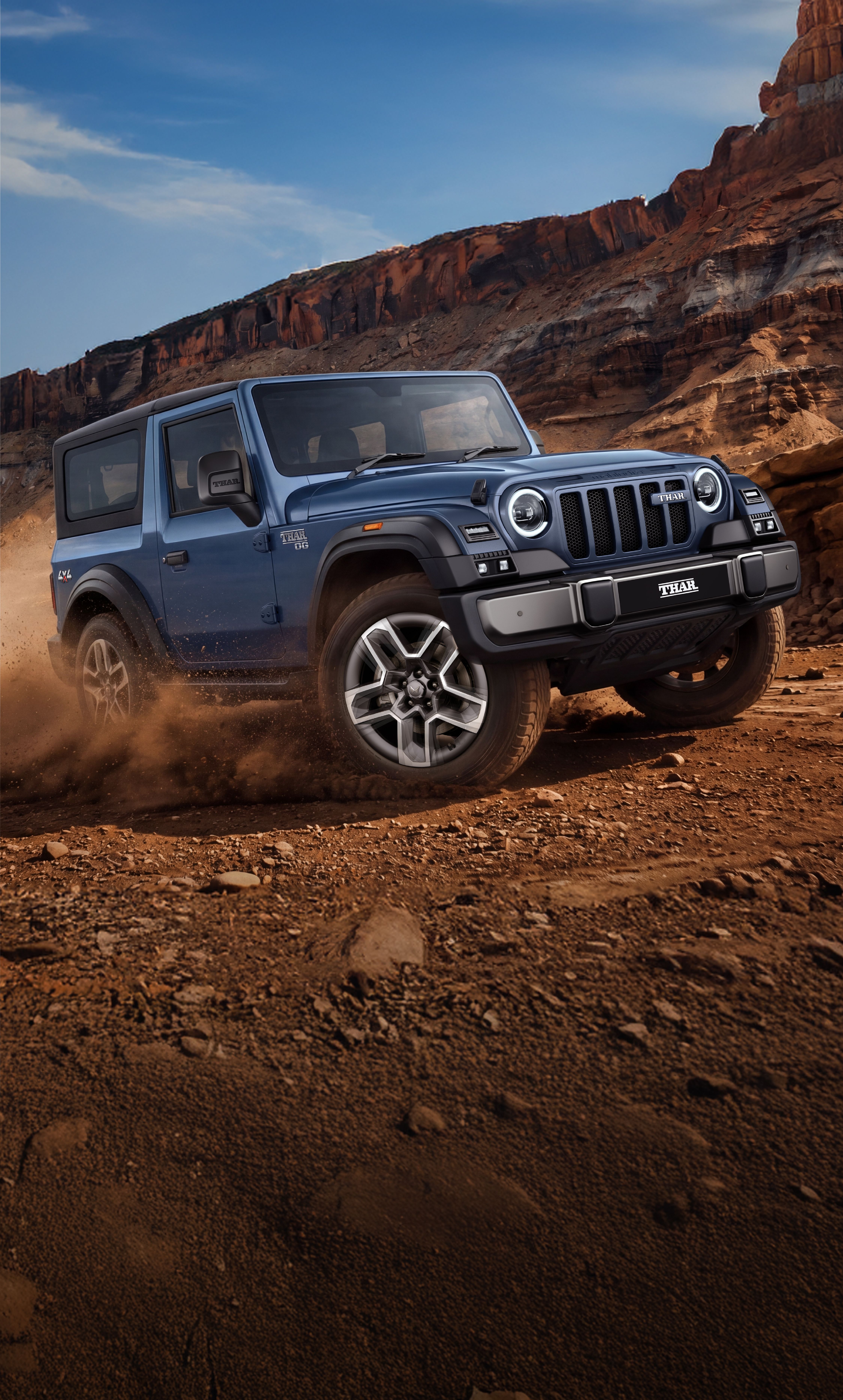 Mahindra Thar OG, Portrait-format version of the same canyon scene: blue Thar OG in front three-quarter view kicking up dust on red rock, 