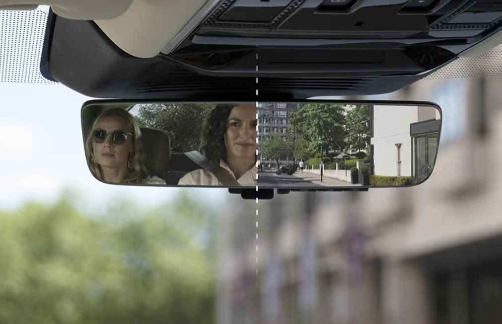 Rearview mirror displaying two passengers and road ahead in vehicle interior.
