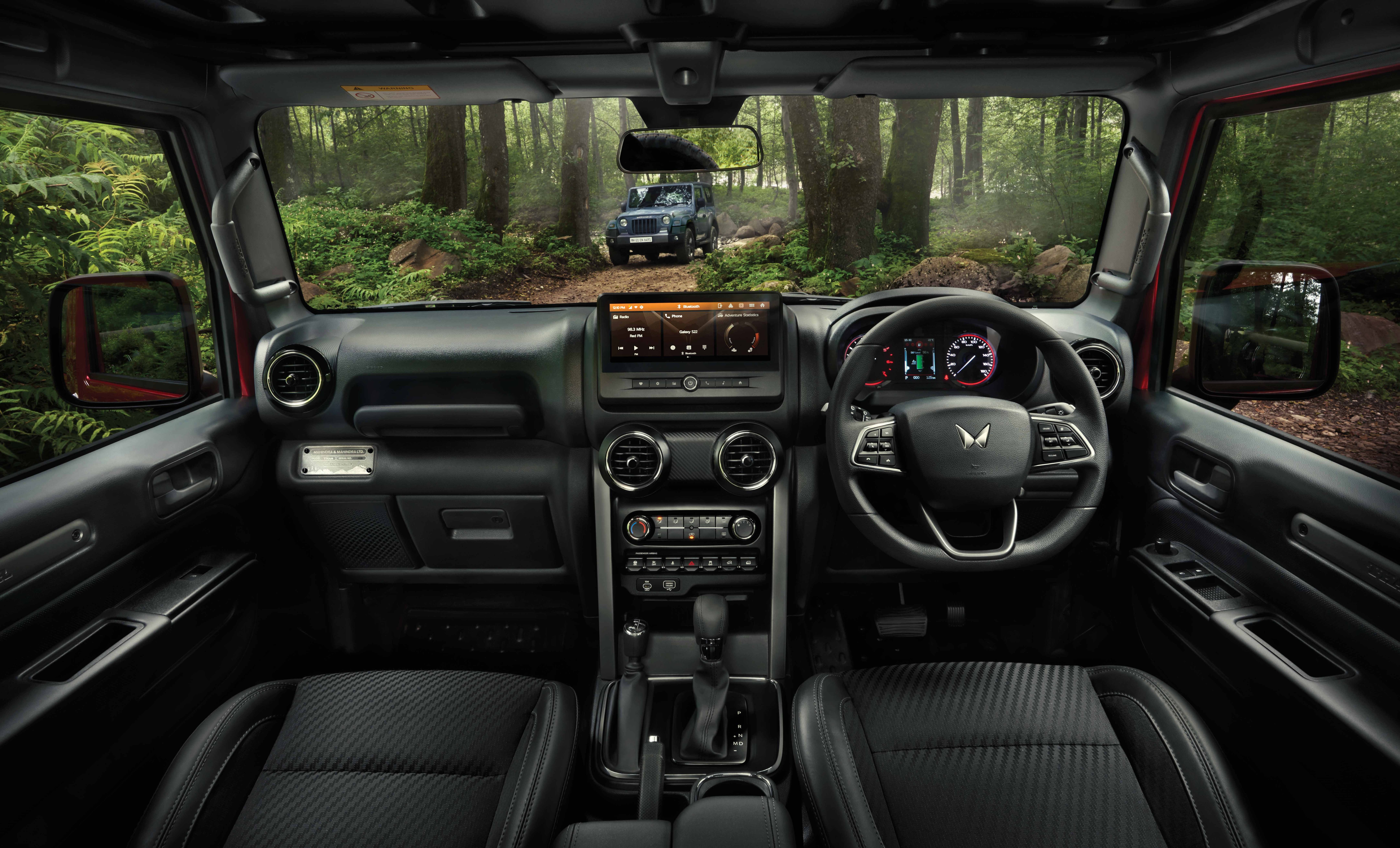 Mahindra Thar OG, Wide front-cabin view from the rear seats: full dashboard, touchscreen showing an amber screen, twin-dial cluster, circu