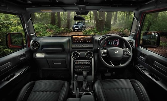 Mahindra Thar OG, Wide front-cabin view from the rear seats: full dashboard, touchscreen showing an amber screen, twin-dial cluster, circu