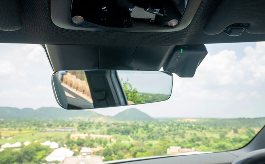 Rearview mirror showing scenic landscape with mountains and green valleys visible through car windows.