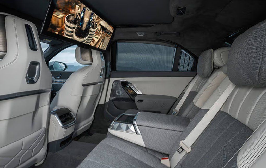Luxury car interior with white and gray seats, dashboard, and overhead display screen.