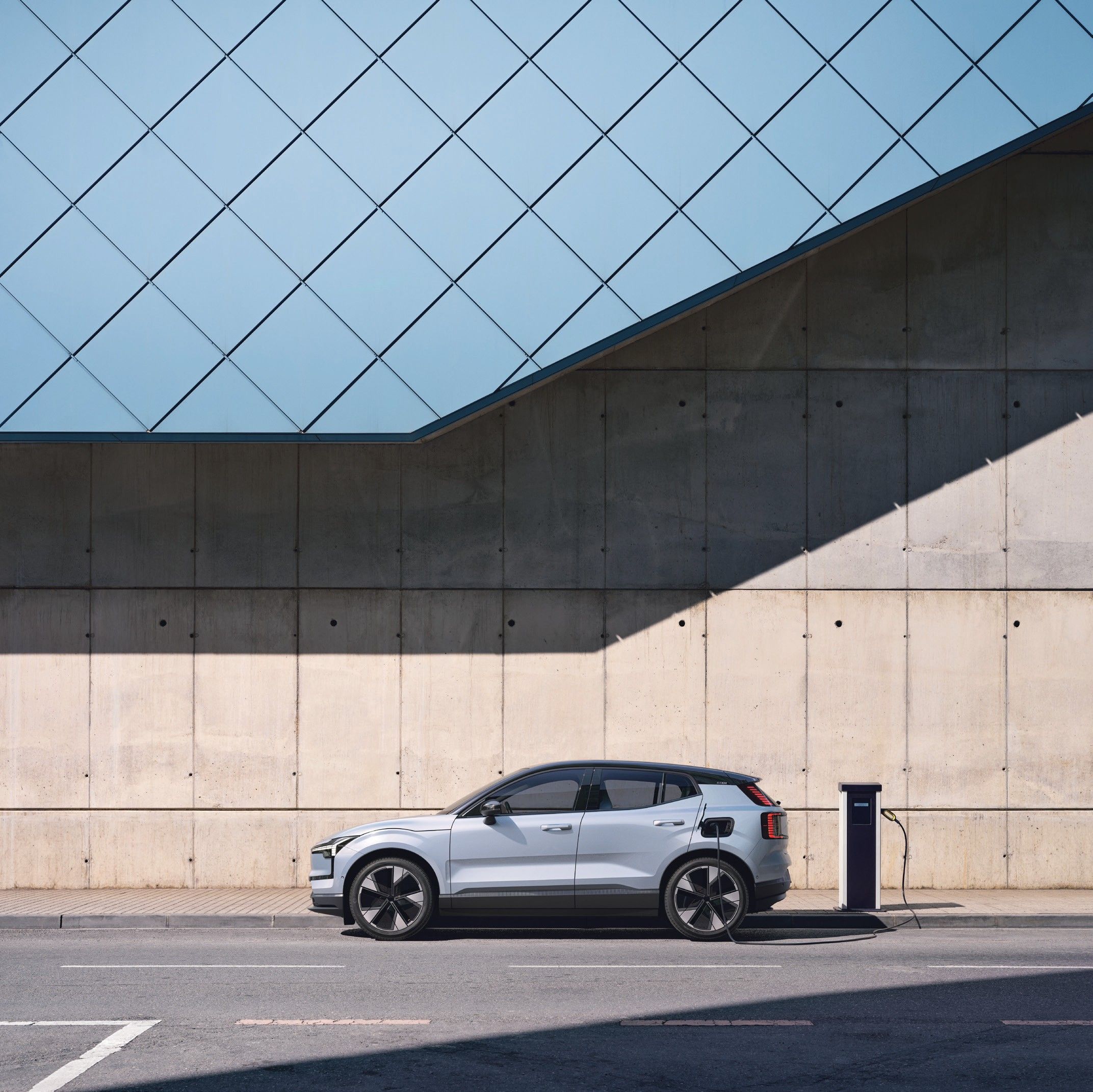 Volvo EX30 — The EX30 parked at a wall-mounted charging station with the charging cable connected.