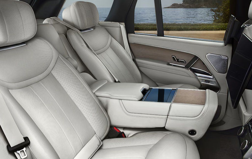 Luxury vehicle rear seats with cream leather upholstery, armrest, and ocean view through windows.