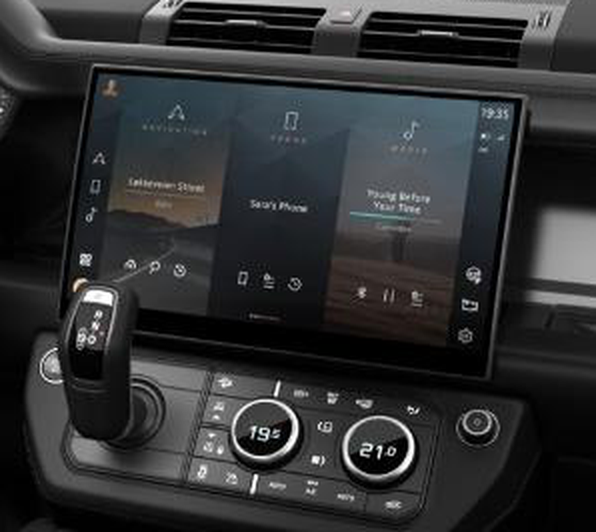 Land Rover Defender — Central Pivi Pro touchscreen infotainment display with navigation, phone and media tiles, set above the dual rotary climate dials and gear selector.