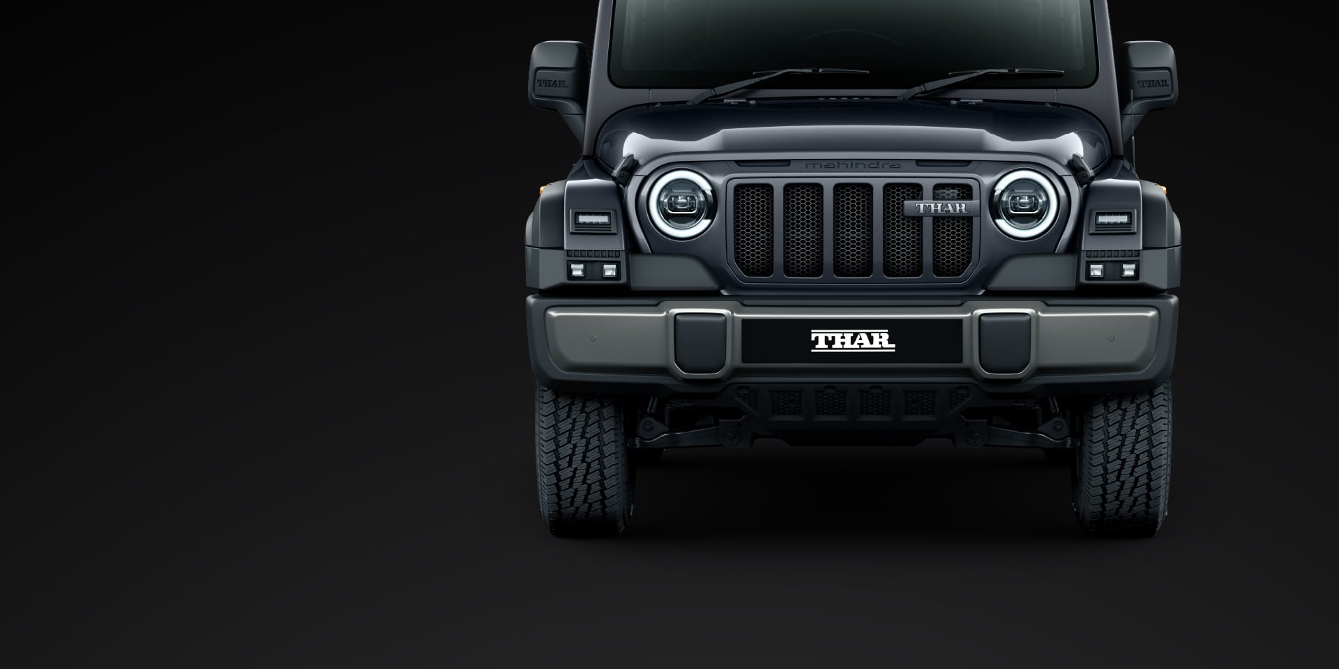 Mahindra Thar OG, Head-on studio shot of a dark grey Thar OG on a black background, showing the seven-slot grille, round LED headlamps wit