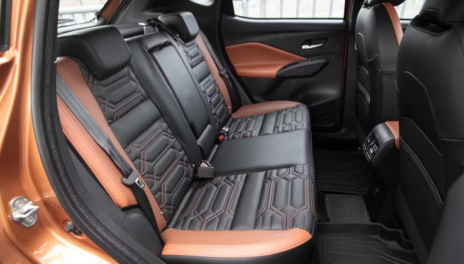 Rear seats of vehicle with black and orange leather upholstery and geometric stitching pattern.