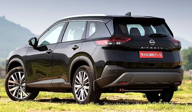 Black Nissan X-Trail SUV parked on grass with mountains in background.