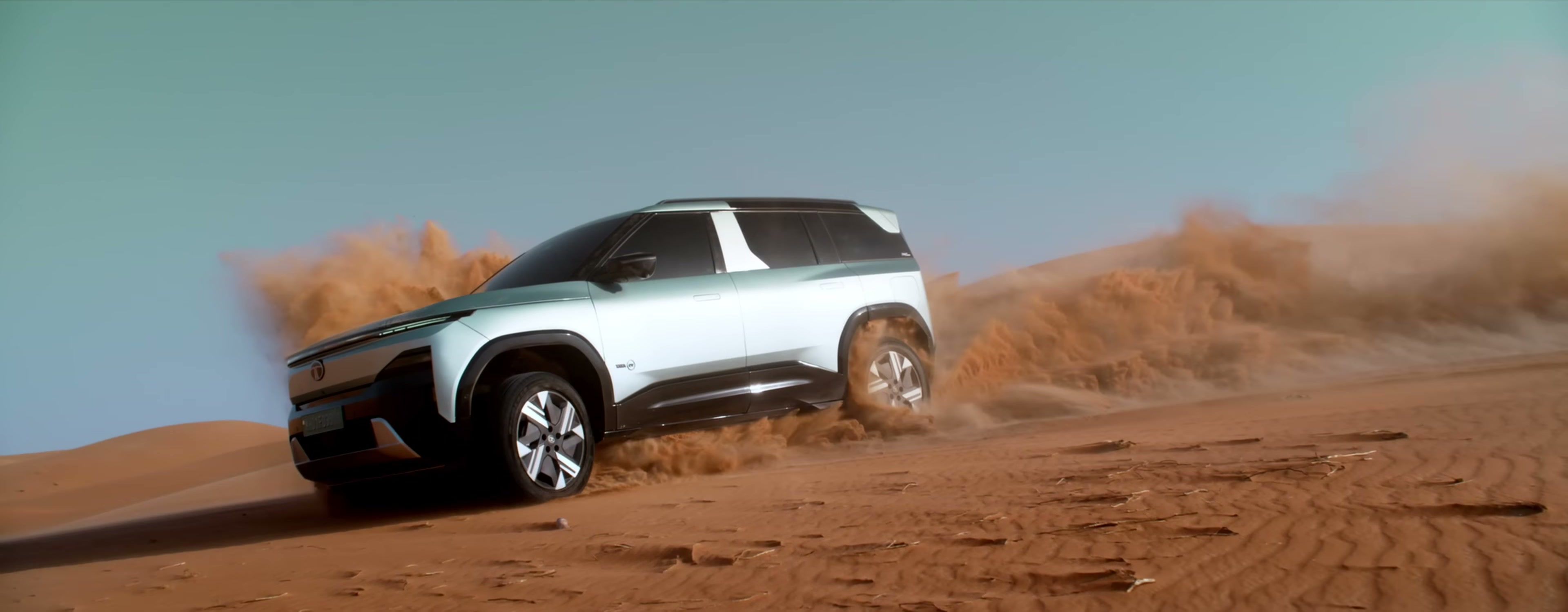 Tata Sierra.ev climbing a sand dune side-on, kicking up sand to demonstrate its QWD dual-motor all-wheel drive