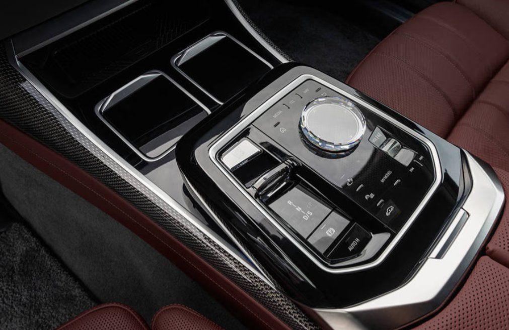 Center console control panel with rotary dial, buttons, and cup holders in luxury sedan.