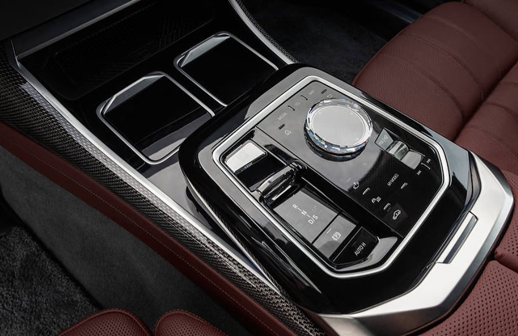 Center console control panel with rotary dial, buttons, and cup holders in luxury sedan.