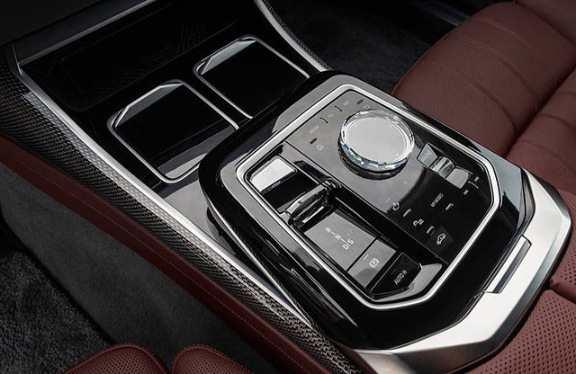 Center console control panel with rotary dial, buttons, and cup holders in luxury sedan.