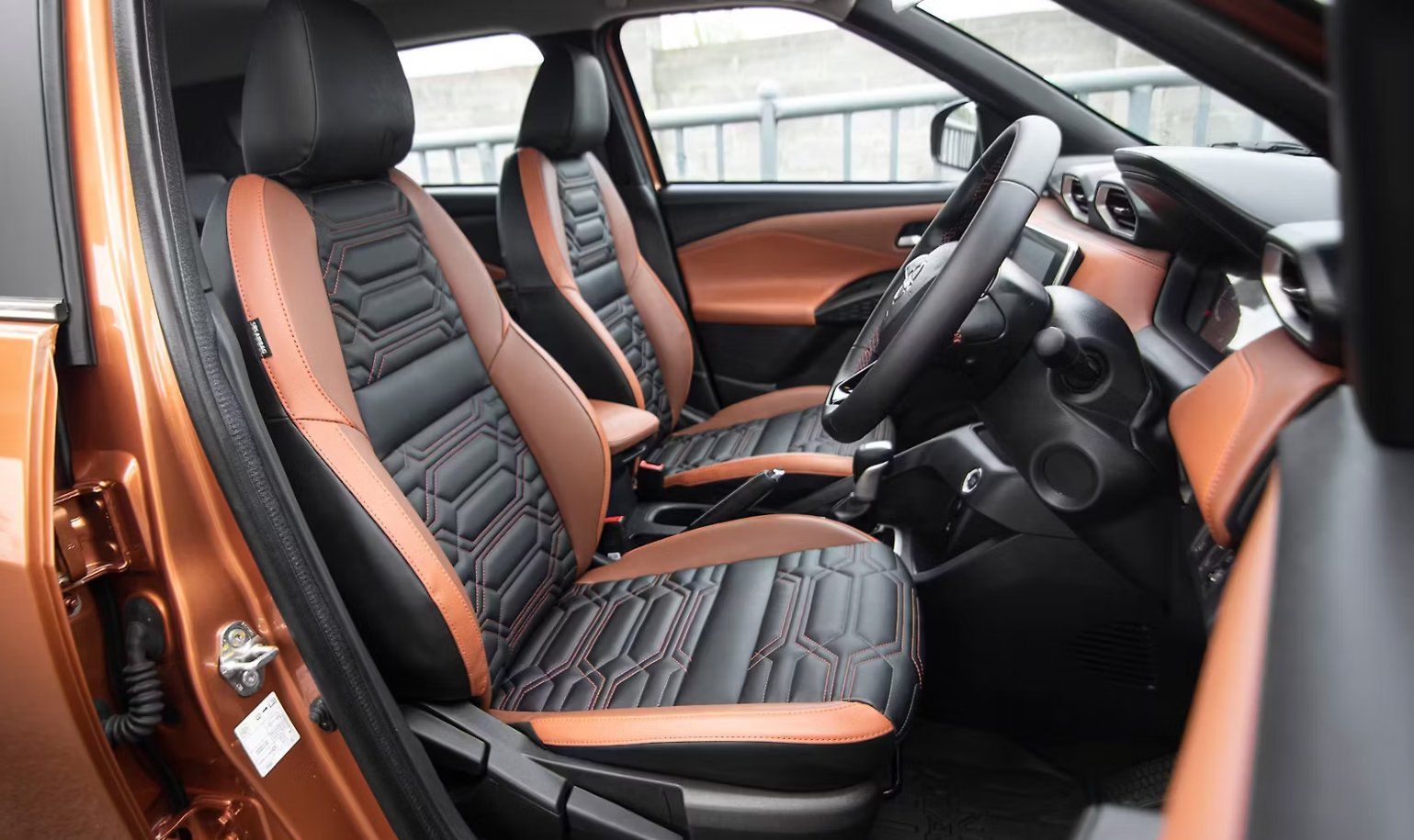 Orange and black leather car interior with steering wheel and dual front seats.