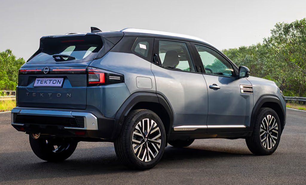 Silver and blue Nissan Tekton SUV parked on asphalt with trees in background.