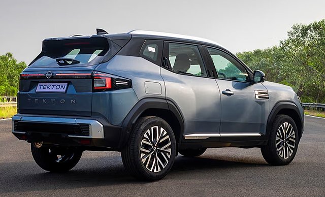 Silver and blue Nissan Tekton SUV parked on asphalt with trees in background.