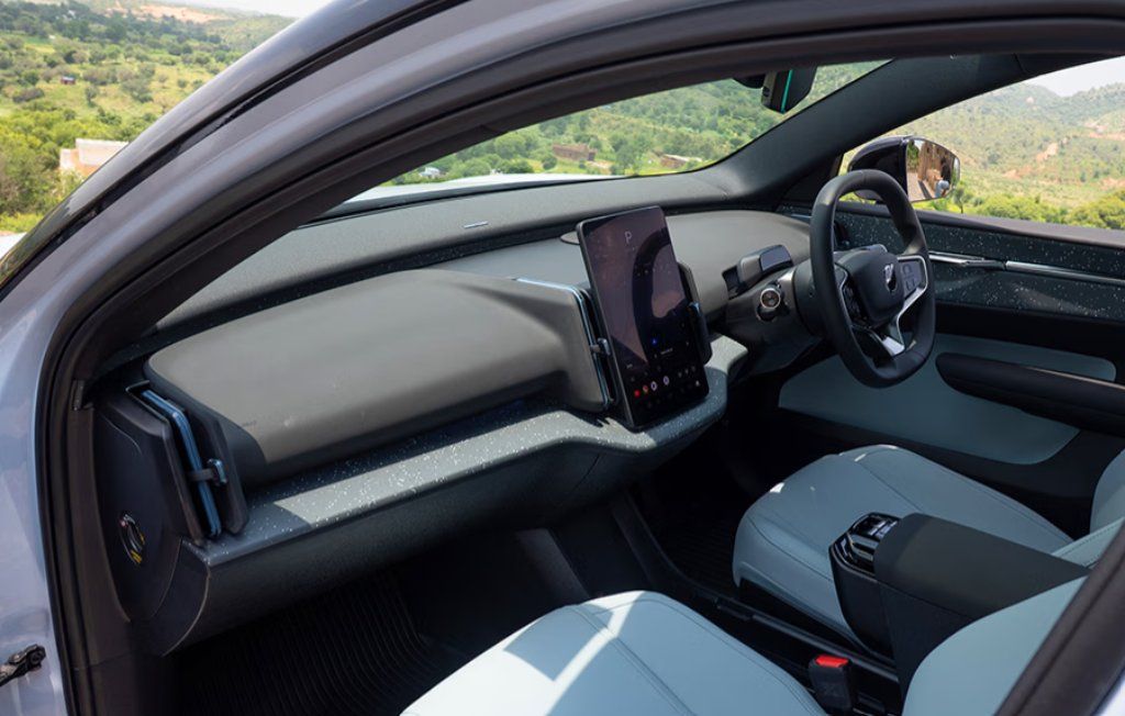 Interior of electric vehicle with dashboard display, steering wheel, and seats overlooking green hillside.