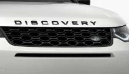 Land Rover Discovery Sport — Gloss-black honeycomb front grille with the DISCOVERY script across the bonnet lip and the Land Rover oval badge at its centre.