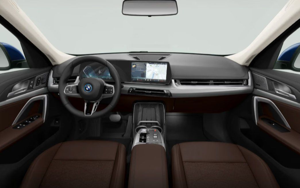 BMW iX1 LWB interior with steering wheel, digital dashboard, and brown leather seats.