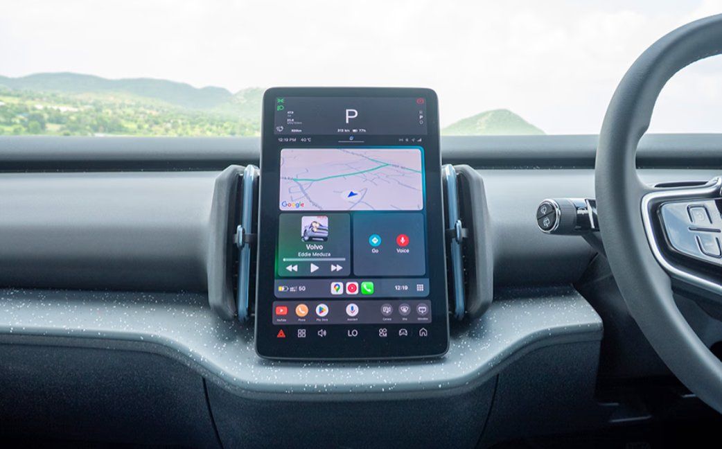 Car dashboard displaying navigation map, apps, and controls with scenic mountain landscape visible through windshield.